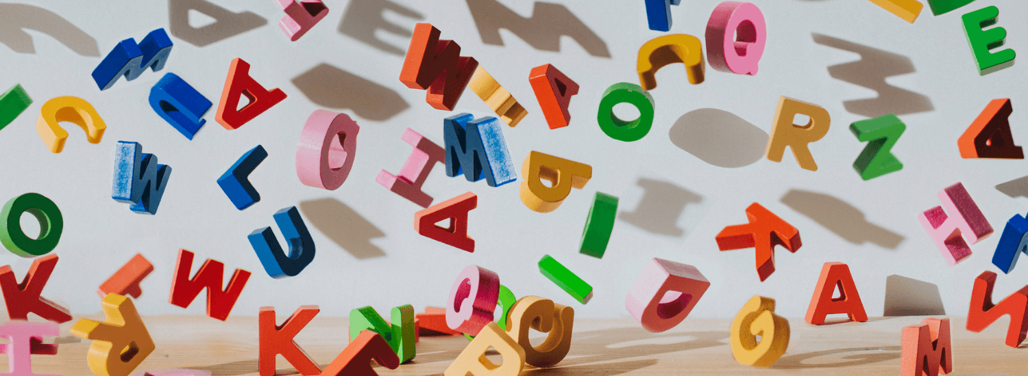 Image of colourful capital letters falling onto a desk, casting shadows on a white wall.